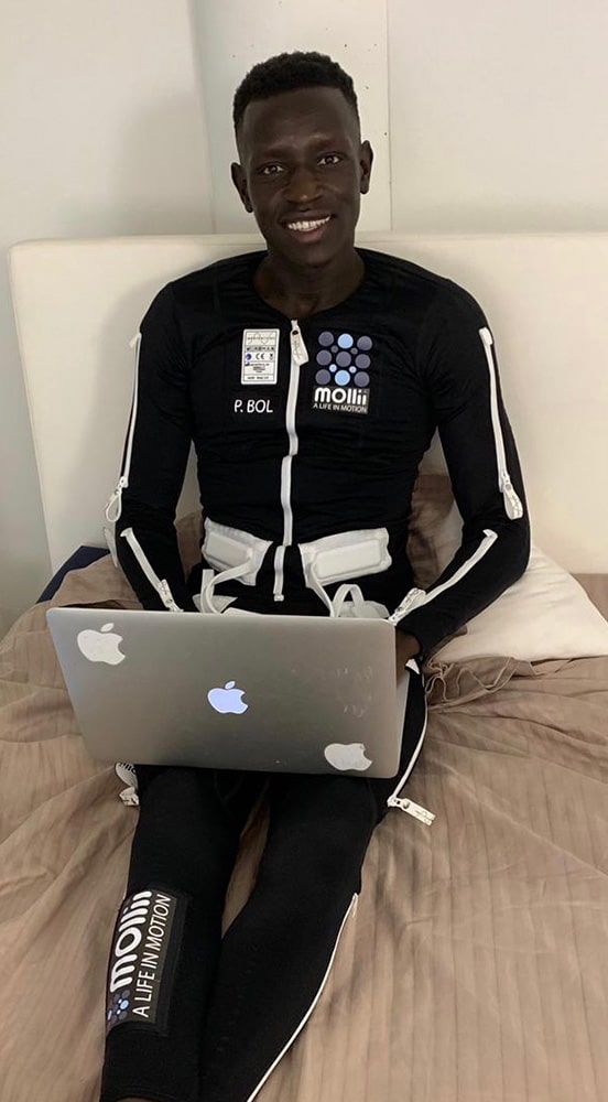 Man Sitting on Bed Wearing Mollii Suit — Wearable Technology - Mollii Exopulse